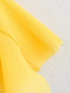 Détail du tissu en mousseline jaune vif montrant une fine texture micro-ridée et des couches