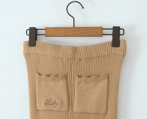 Dettaglio dei pantaloni in maglia cammello con ricamo Lucky e bordi all'uncinetto