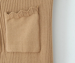 Dettaglio del cardigan in maglia color cammello con trama a coste e bordo a smerlo