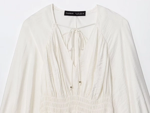 Detail of white satin V-neck top showing smocked waist and drawstring metal tips