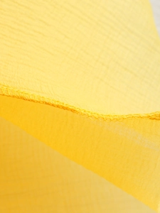 Détail macro du tissu mousseline jaune montrant la couture surjetée et la texture fine