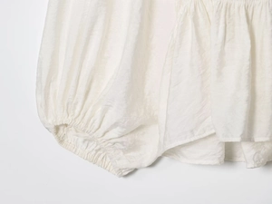Detail of white pleated shirt showing puff sleeves and elastic cuffs with fine texture