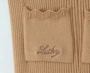 Dettaglio della tasca in maglia color cammello con ricamo Lucky e bordi a uncinetto
