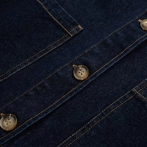 Macro detail van donkerblauwe denim stof met oranje stiksels en schildpadpatroon knoop