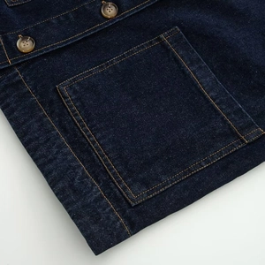 Detail van donkerblauw denim jack met twillzak en contrasterende gele stiksels