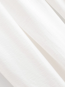 Détail macro du tissu en lin blanc respirant montrant la texture tissée et les plis doux