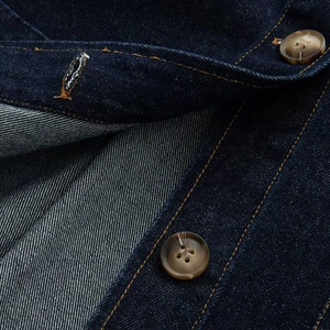 Detail van amberkleurige harsknoop en contraststiksels op een blauw spijkerjack