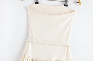 Detail view of cream strapless dress with waist belt and pleated ruffle hemline