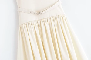 Detail of cream strapless dress featuring slim buckled waist belt and fine pleated skirt