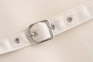 Detail of beige canvas waist belt with silver metal eyelets and square buckle