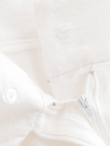 Détail du pantalon en lin blanc montrant le bouton et la fermeture éclair en métal