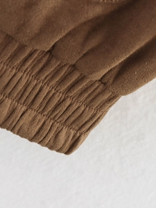 Macro view of brown suede bomber jacket showing elastic waistband and ribbed texture