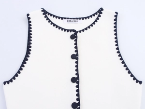 Detail of white knit vest with navy scalloped edges and decorative round buttons