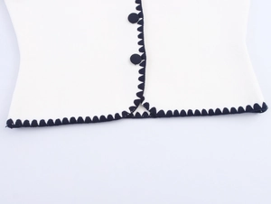 Close-up of white knit vest with navy wavy trim and matching buttons on the hem