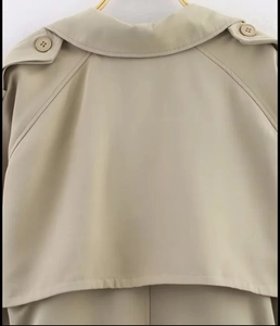 Detail of khaki trench coat back featuring wind flap, shoulder straps and stitching