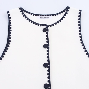 Women's white sleeveless knit vest featuring black scallop trim and button details