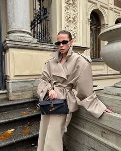 Detail of khaki cropped trench coat with waist tie and black leather clutch bag