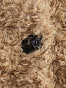 Gros plan sur la texture bouclée en fausse fourrure camel et un bouton en cuir noir