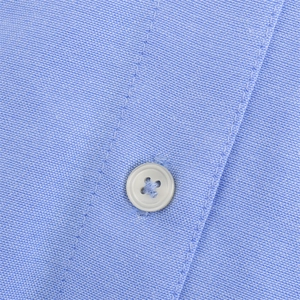 Macro detail of light blue Oxford shirt fabric with white buttons and fine stitching