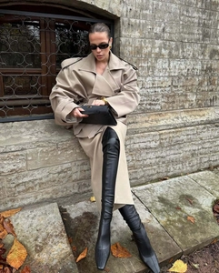 Detail of a khaki belted trench coat paired with black leather over-the-knee high heel boots