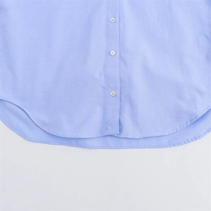 Detail of light blue cotton shirt with curved hem, resin buttons and fine stitching
