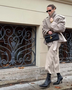 Detail of beige oversized wool coat paired with straight skirt and black accessories