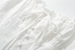 Dettaglio di un abito francese in cotone bianco con ricamo floreale e scollatura a bottoni