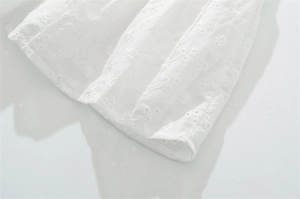 Dettaglio di abito in cotone bianco con ricamo a margherita traforato e cuciture fini