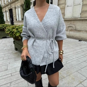 Women's light grey wrap knit cardigan with V-neck and tie-waist in a stylish urban setting