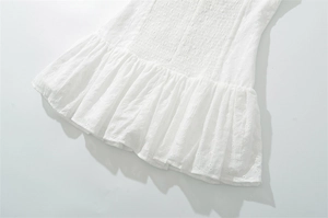 Dettaglio di un abito in cotone bianco con ricamo floreale traforato e orlo a balze smock