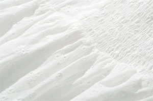 Dettaglio macro del cotone bianco con ricamo a margherita e lavorazione a punto smock