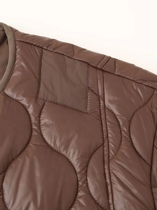 Détail macro d'une veste matelassée marron foncé montrant la texture et les coutures courbes