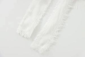 Detail of white sequin top featuring delicate tassel trim and sheer mesh fabric texture