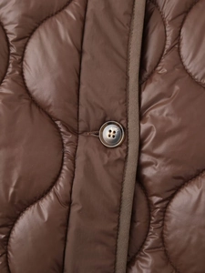 Détail d'une veste matelassée marron café avec bouton rond et motif de surpiqûres