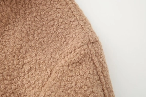 Detailed macro view of camel faux shearling texture and precision stitching on the jacket pocket