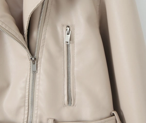 Detail of silver zippers and fine faux leather texture on an off-white biker jacket