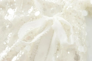 Detail of white sequin fabric with soft chiffon bow and delicate raw edge stitching