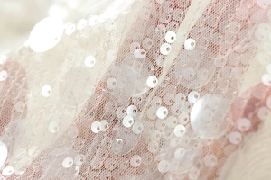 Macro view of light pink sequin mesh fabric with iridescent round paillettes