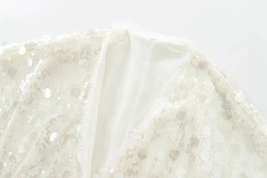 Detail of white sequined V-neck top with fuzzy feather trim and mesh fabric texture