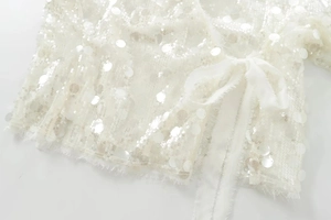 Detail view of white sequined fabric with fringe trim and an elegant side ribbon tie