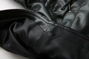 Detailaufnahme einer schwarzen Kunstlederjacke mit Nähten und Metallösen im Detail