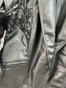 Detail der schwarzen Kunstlederjacke mit Schnürung und Metallösen am Revers der Jacke