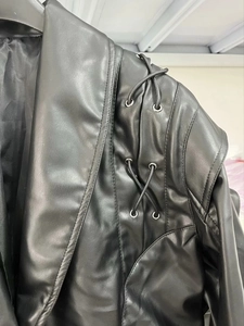 Detail einer schwarzen Kunstlederjacke mit Metallösen und Schnürung an der Schulter