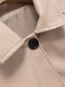 Detail of beige faux leather coat featuring a round button and high-quality stitching