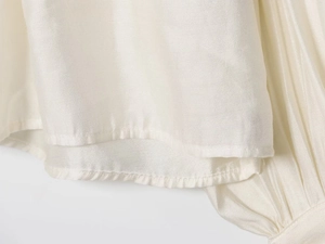 Detailed close-up of cream draped blouse featuring high-quality silk texture and pleated hem