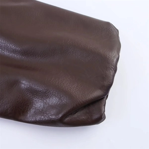 Détail d'une veste en simili cuir marron foncé montrant la texture grainée et les finitions