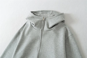 Détail d'un sweat à capuche gris zippé avec col montant et tissu en coton texturé