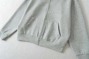 Détail du sweat à capuche gris zippé montrant la texture en coton et les poches
