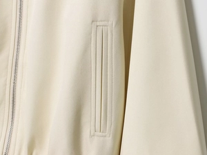 Detail shot of a cream jacket featuring a silver metal zipper and welt pocket stitching