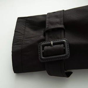 Detailed close-up of a black trench coat cuff featuring a decorative buckled strap